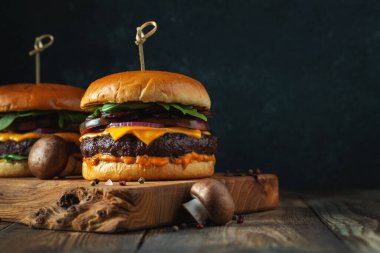 Eski ahşap bir masada iki lezzetli ev yapımı sığır eti, peynir ve mantar burger. Yağlı, sağlıksız yiyecekler. Kopyalama alanı ile.