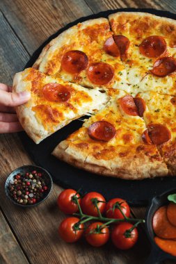 Bir dilim peynirli sıcak İtalyan pizzası. Koyu ahşap arka planda pizza sosisi..