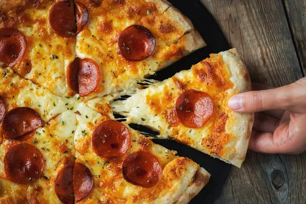 Bir dilim peynirli sıcak İtalyan pizzası. Koyu ahşap arka planda pizza sosisi..