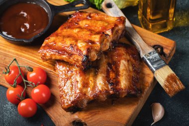 Baharatlı, ızgara pirzola. Barbekü, acı biber ve taze domatesle servis edilir. Eski bir ahşap kesim tahtasının üzerinde.
