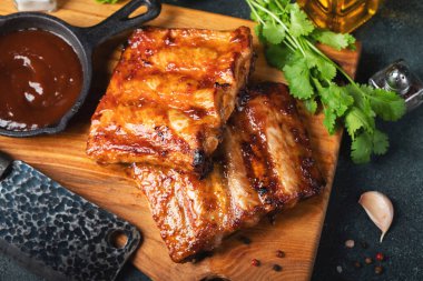 Baharatlı, ızgara pirzola. Barbekü, acı biber ve taze domatesle servis edilir. Eski bir ahşap kesim tahtasının üzerinde.