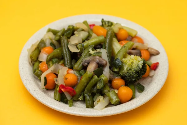 Mixed boiled vegetables on light brown dish on yellow