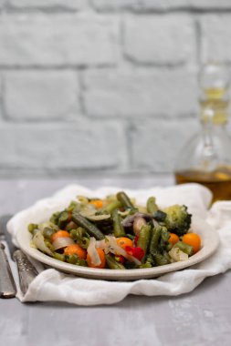 Açık kahverengi tabakta seramikte haşlanmış sebzeler.