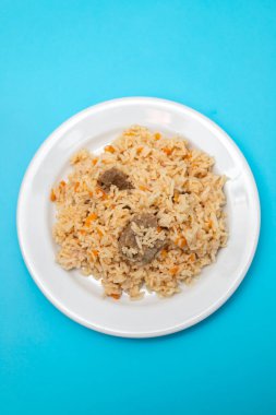 Rice with vegetables and meat on white plate on blue