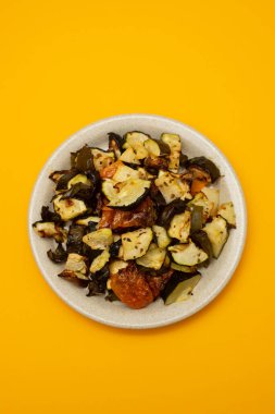 Mixed baked vegetables on light brown dish on yellow