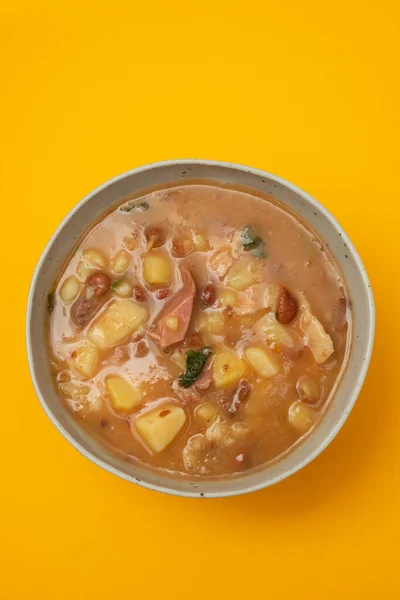 Sopa de pedra Portuguese Stone Soup with beans and sausages in the plate on yellow paper.