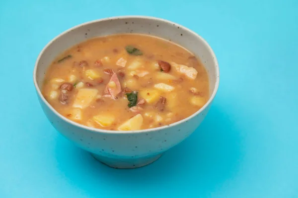 Sopa de pedra Portuguese Stone Soup with beans and sausages in the plate on blue paper.
