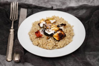 Cooked quinoa with vegetables and white sauce on white plate