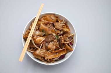 Fried noodles with vegetables and beef in white bowl on ceramic