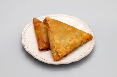 Two samosas with meat and vegetables on white small plate