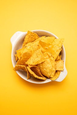 Few mexican nachos chips in small bowl on yellow