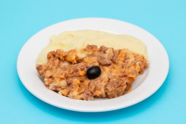 Minced meat and mashed potato on white plate on blue