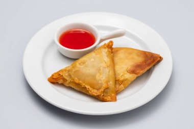 Two samosas with meat and vegetables on white small plate