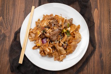 Fried noodles with vegetables and beef in white dish on brown