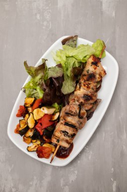 Baharatlı, sebzeli ve beyaz tabakta taze salatalı ızgara et.