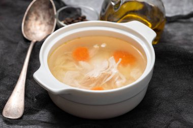 bowl of chicken broth with chicken and carrot with spoon in dark