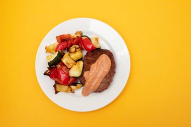 Soslu hamburger eti ve beyaz tabakta sebze.