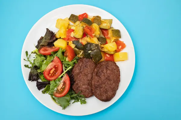 three fried ground meat with vegetables and fresh salad on white plate on ceramic