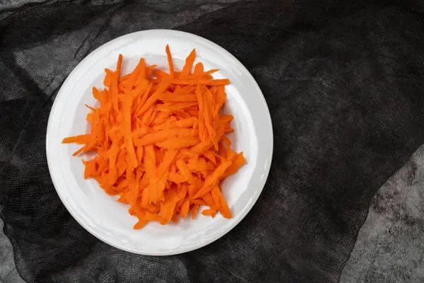 Shredded fresh uncooked carrot on white small plate