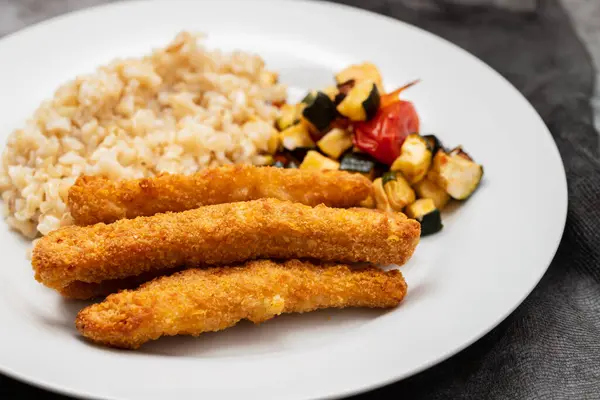 Breaded chicken strips with rice and vegetables. Chicken fingers.