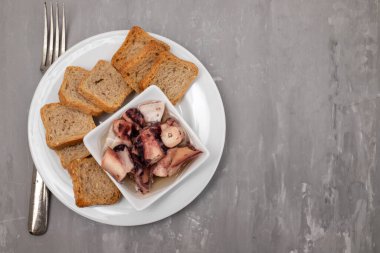 küçük kasede yağlı ahtapot salatası ve beyaz tabakta tost.