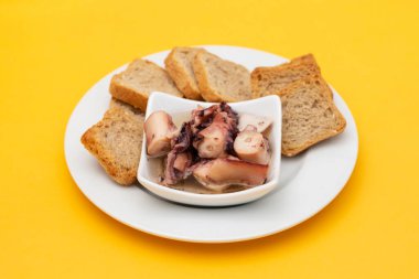 küçük kasede yağlı ahtapot salatası ve beyaz tabakta tost.