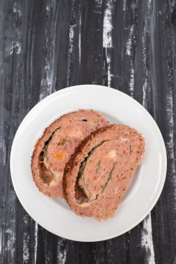 Dilimlenmiş rulo köfte ve ıspanak yakından beyaz bir tabakta.