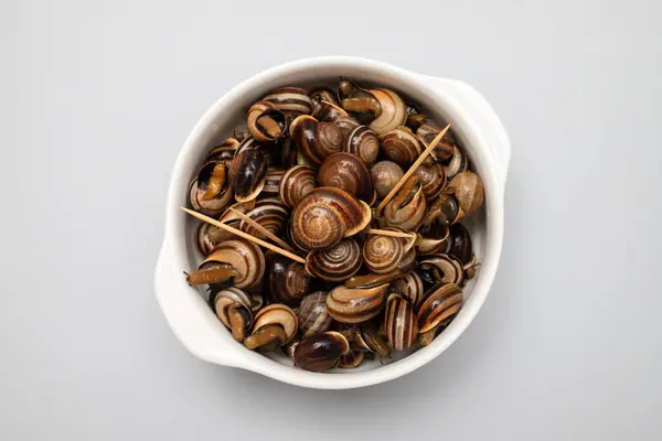 stock image boiled snails with herbs in the white bowl on yellow background