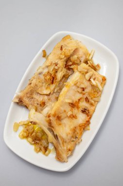 Beyaz tabakta soğan ve biberli kızarmış morina balığı.