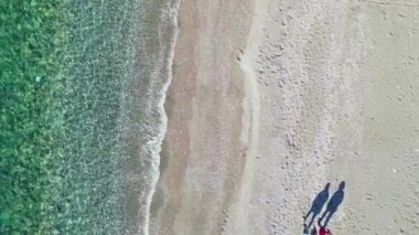 Kumsalda turkuaz deniz kenarında yürüyen iki kadın.