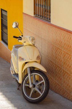 Bir binanın yanındaki dar bir İspanyol caddesinde park etmiş bir scooter, bir şehir aracı.