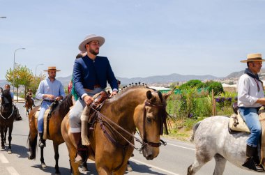 NERJA, SPAIN - 15 Mayıs 2022 Flamenko elbiseli kadınlar ve Endülüs atlarındaki erkekler en iyi geleneksel halk kostümleri ve festival töreninde yer alan geniş kenarlı şapkalar giydiler.