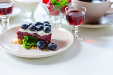 Fırında vanilya ve çilek aromalı cheesecake, sindirim bisküvisi kırıntısında yabanmersini sosu ve tatlı.