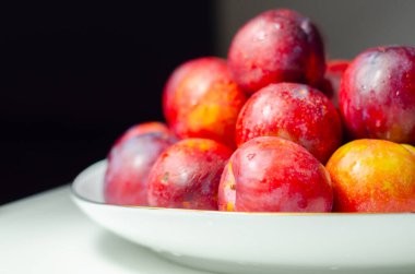 Üzerinde kırmızı erikler olan beyaz bir tabak. Erikler öyle bir sıralanmış ki, yenmeye hazırmış gibi görünüyorlar. Tabak bir masaya konur ve masa da beyazdır.