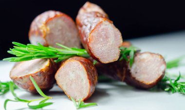 Üstünde biberiye olan bir yığın sosis. Sosisler ikiye bölünmüş ve piramit şeklinde düzenlenmiş.