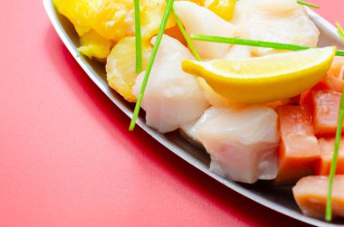 Metal tepside bir tabak deniz ürünü ve limon. Tabak farklı balık türleriyle dolu.