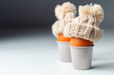 Üzerinde fincanlar olan turuncu yumurtalar. Şapkalar örülmüş ve ponponları var.