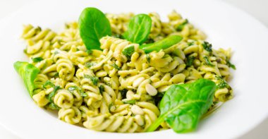 Üstünde ıspanak olan bir tabak makarna. Ispanak taze ve yeşildir ve makarna pişirilir ve yenmeye hazırdır. Yemek sağlıklı ve lezzetli görünüyor.