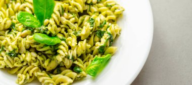 Üstünde ıspanak olan bir tabak makarna. Ispanak taze ve yeşildir ve makarna pişirilir ve yenmeye hazırdır. Yemek sağlıklı ve lezzetli görünüyor.