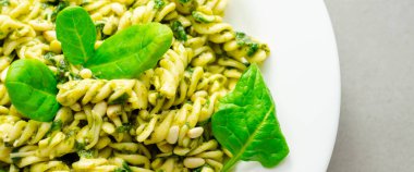 Üstünde ıspanak olan bir tabak makarna. Ispanak taze ve yeşildir ve makarna pişirilir ve yenmeye hazırdır. Yemek sağlıklı ve lezzetli görünüyor.