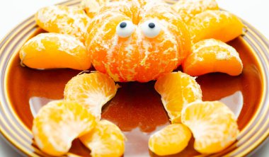 Dilimlerden yapılmış yengeç desenli bir tabak portakal dilimi. Yengecin iki gözü var ve kahverengi bir tabakta oturuyor.