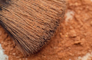 Makyaj fırçası toz yığınının üzerinde duruyor. Fırça siyah ve sarı ve toz kahverengi. Yaratıcılık ve kendini ifade etme kavramı, makyajın kişinin görünüşünü iyileştirmek için sık sık kullanıldığı gibi.