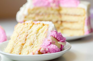 Beyaz tabakta pembe kremalı bir dilim pasta. Pasta katmanlar halinde kesilmiş ve üstünde pembe bir krema var.