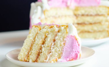 Beyaz tabakta pembe kremalı bir dilim pasta. Pasta katmanlar halinde kesilmiş ve üstünde pembe bir krema var.