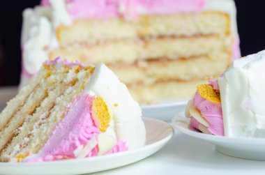 Beyaz tabakta pembe kremalı bir dilim pasta. Pasta katmanlar halinde kesilmiş ve üstünde pembe bir krema var.