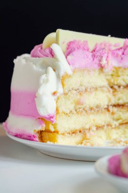 Beyaz tabakta pembe kremalı bir dilim pasta. Pasta katmanlar halinde kesilmiş ve üstünde pembe bir krema var.