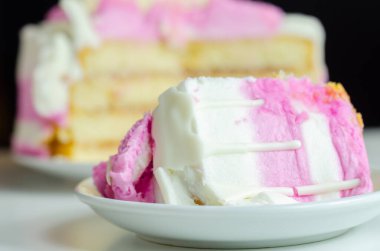 Beyaz tabakta pembe kremalı bir dilim pasta. Pasta katmanlar halinde kesilmiş ve üstünde pembe bir krema var.