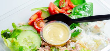 Siyah kaşıklı ve sarı soslu bir salata. Salata domates, salatalık ve ıspanak içeren sebzelerle dolu.