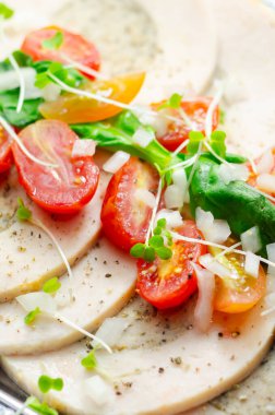 Bir tabak dolusu sebze ve et. Sebzeler arasında domates, soğan ve yeşil biber yer alıyor. Yemek maydanozla süslenmiş, kumaş ve renklerin karışımı var.