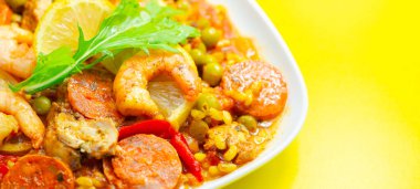 Bir tabak karides, biber ve pilav. Tabak sarı bir masada servis edilir.